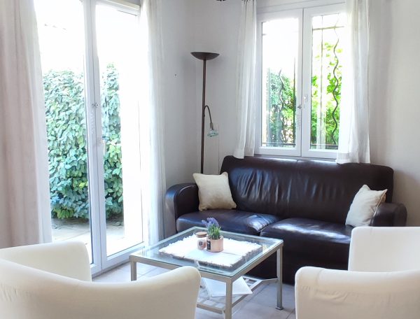 Salon lumineux avec canapé confortable, grande baie vitrée offrant une vue sur le jardin, et décoration moderne et épurée.